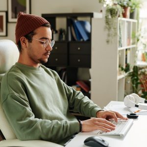 Serious guy in casualwear typing on keyboard while sitting in front of computer