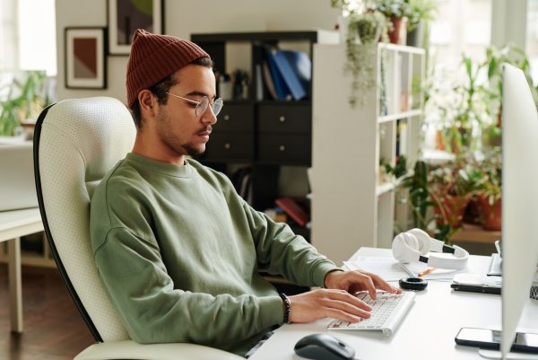 Serious guy in casualwear typing on keyboard while sitting in front of computer