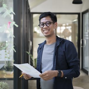 Young creative man standing in modern office and smiling to camera.