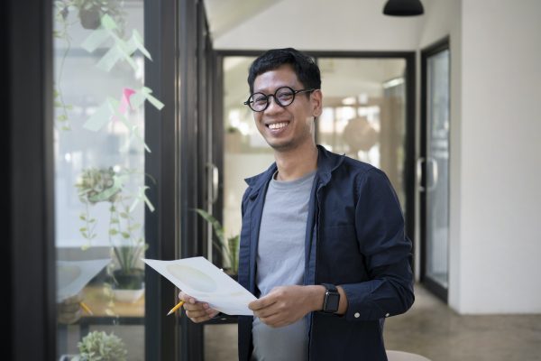 Young creative man standing in modern office and smiling to camera.