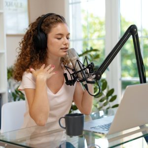 Young curly female recording podcast from home and talking into a microphone