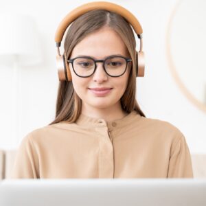 Young woman wearing and wireless headphones, sitting in front of open laptop at home