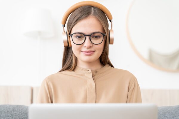 Young woman wearing and wireless headphones, sitting in front of open laptop at home